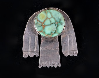 May include: A silver pendant with a green turquoise stone in the center. The pendant is shaped like a stylized bird with outstretched wings.