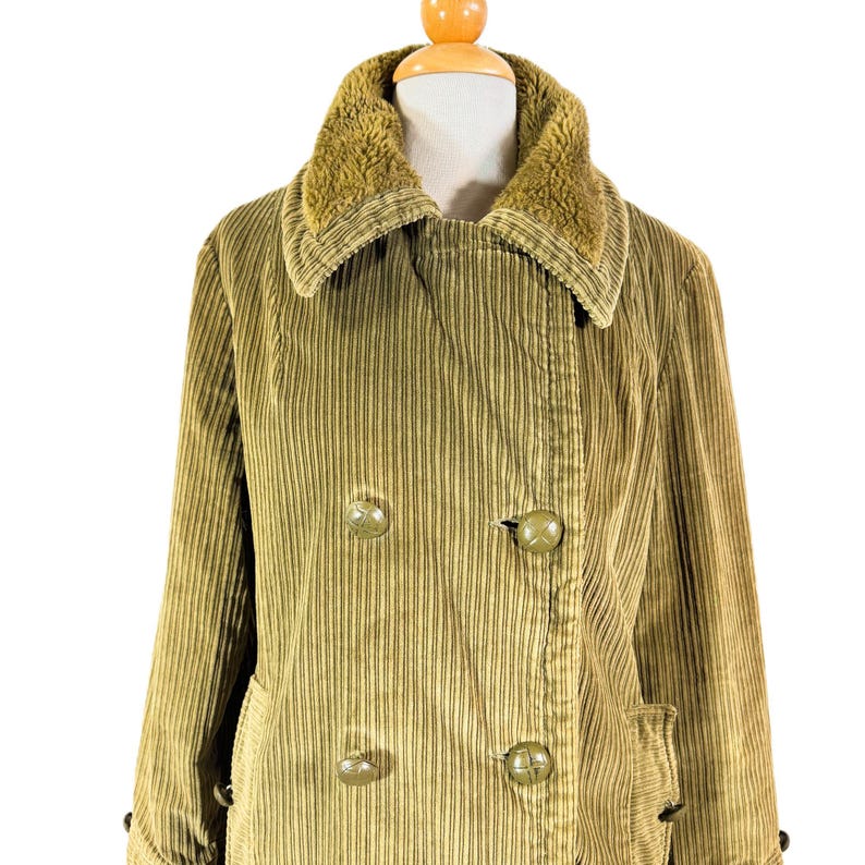 May include: A vintage olive green corduroy coat with a faux fur collar. The double-breasted coat features large, round buttons and two front pockets. The coat is displayed on a mannequin.