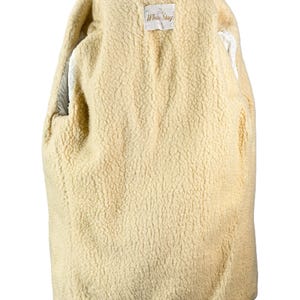 May include: A cream-colored, lined coat with a textured interior and a dark green collar. The coat is displayed on a hanger, showcasing the interior lining and the "White Stag" label.