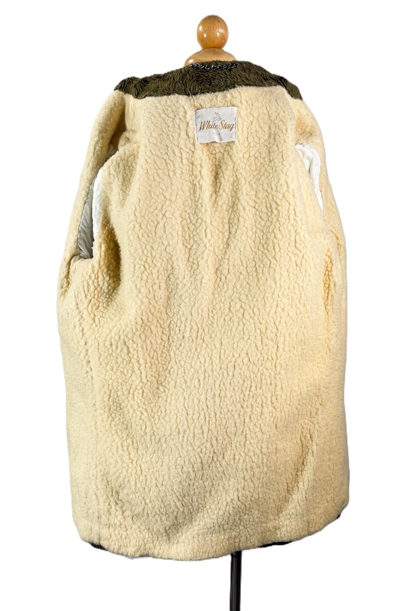 May include: A cream-colored, lined coat with a textured interior and a dark green collar. The coat is displayed on a hanger, showcasing the interior lining and the "White Stag" label.