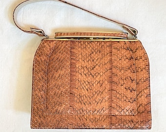 Peut inclure: Un sac à main vintage marron avec un motif peau de serpent. Le sac a une forme rectangulaire avec un dessus incurvé et une poignée. Le fermoir et les attaches de la poignée sont de couleur dorée. Les mots "front view" sont en bas de l'image.