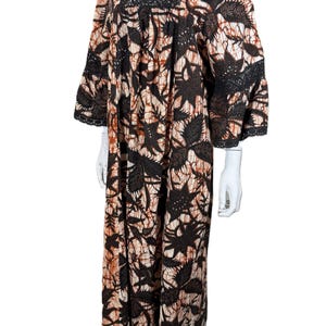 May include: A floor-length dress featuring a brown and cream batik-style leaf pattern. The garment has a square neckline, three-quarter length sleeves, and black lace trim detailing along the neckline and the edges of the sleeves.