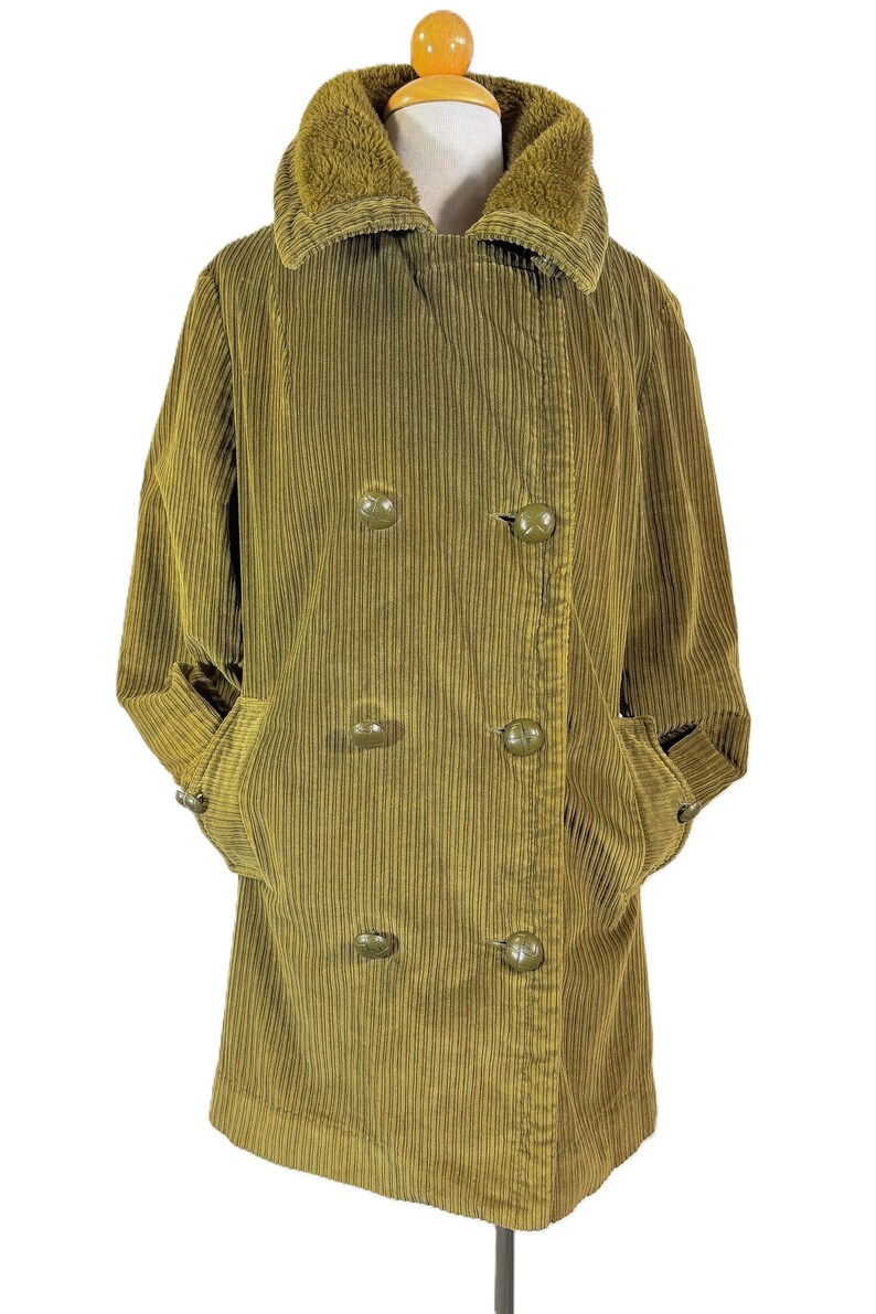 May include: Olive green corduroy coat with a faux fur collar. The double-breasted coat features large, round buttons and pockets. The sleeves are cuffed, and the coat is displayed on a mannequin.