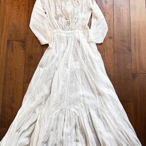 May include: A white vintage dress with long sleeves, a high neckline, and intricate lace detailing. The dress features a fitted bodice and a flowing skirt, showcasing a classic, elegant design. The dress is made of a lightweight fabric.