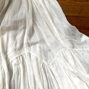 May include: A white, flowing skirt with intricate lace detailing. The fabric appears lightweight and airy, with a delicate pattern along the hem and seams. The skirt is gathered, creating soft folds and a romantic aesthetic.