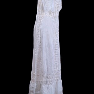 May include: A white vintage dress with intricate lace detailing. The dress features a high neckline, short sleeves, and a flowing skirt. The dress is made of a lightweight fabric and has a delicate, feminine appearance. The dress is a classic example of vintage fashion.