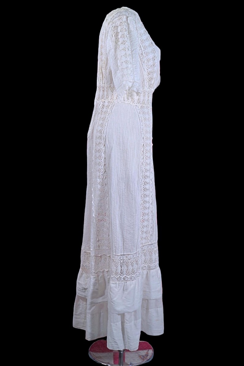 May include: A white vintage dress with intricate lace detailing. The dress features a high neckline, short sleeves, and a flowing skirt. The dress is made of a lightweight fabric and has a delicate, feminine appearance. The dress is a classic example of vintage fashion.