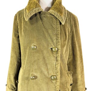 May include: A corduroy coat in a muted olive green color, featuring a double-breasted design with large, round buttons. The coat has a plush, textured collar and side pockets. The garment is displayed on a mannequin.