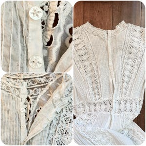 May include: Close-up of a white vintage blouse with intricate lace detailing and decorative buttons. The blouse features vertical pleats and a high neckline, showcasing a delicate, textured design. The fabric appears to be lightweight and semi-sheer.