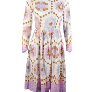 May include: A white dress with a long sleeve and a floral print. The print features a patchwork design with purple, pink, brown, and blue flowers. The dress has a fitted bodice and a full skirt.