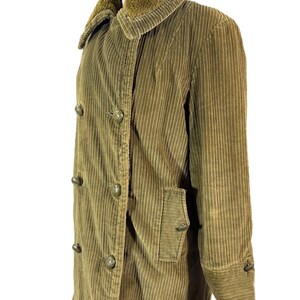 May include: A corduroy coat in olive green, displayed on a mannequin. The coat features a double-breasted design with large, round buttons and a plush, brown faux-fur collar. It has a pocket on the front and buttoned cuffs.