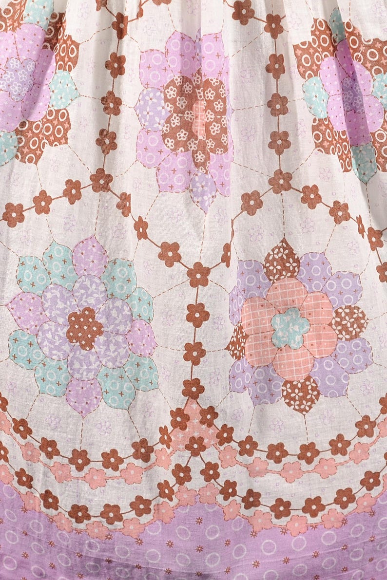 May include: White fabric with a repeating pattern of brown, pink, and purple flowers. The flowers are made up of smaller patchwork pieces. The fabric has a light, airy feel.