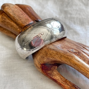 Puede incluir: Un brazalete de plata con un diseño geométrico. El brazalete está hecho de metal y tiene un acabado brillante.