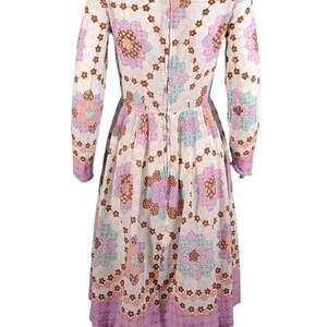 May include: A white dress with a pink, brown, and blue floral pattern. The dress has long sleeves and a fitted bodice. The skirt is full and flows out from the waist.