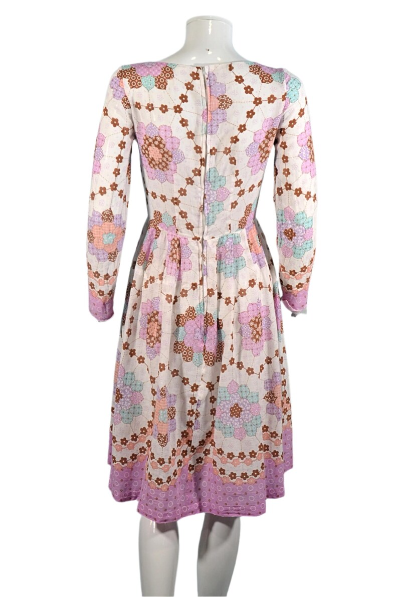 May include: A white dress with a pink, brown, and blue floral pattern. The dress has long sleeves and a fitted bodice. The skirt is full and flows out from the waist.