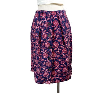 May include: A navy blue skirt with a floral pattern in shades of pink and white. The skirt features a button-down front and a pleated design. The skirt is knee-length and appears to be made of a lightweight fabric.