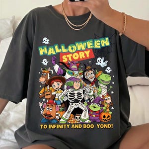 May include: A charcoal gray t-shirt featuring a graphic print of animated characters dressed in Halloween costumes. The text reads HALLOWEEN STORY at the top and TO INFINITY AND BOO-YOND! at the bottom, surrounded by ghosts, pumpkins, and a spiderweb.
