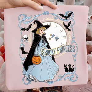 May include: A light pink fabric item featuring a graphic of a blonde character in a blue gown and black witch hat, holding an orange pumpkin bucket. The design includes a clock face, bats, a skull, black boots, two black cats, and the text SPOOKY PRINCESS.