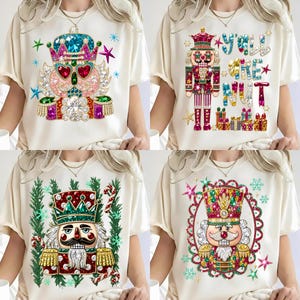 May include: A set of four cream-colored t-shirts, each featuring a different graphic of a nutcracker decorated with colorful, sparkling gemstone-like patterns, stars, snowflakes, and the text Y'ALL ARE NUT on one of the designs.