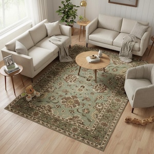 May include: An overhead shot of a living room setup featuring a large, rectangular rug with a floral pattern in shades of green, brown, and cream. Two beige sofas, a matching armchair, and a round coffee table are arranged on the rug. Small side tables and decorative items complete the scene.