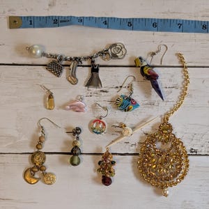 May include: A selection of earrings and charms, including a gold-coloured headpiece, a parrot earring, and a charm bracelet with a high heel and dress. A measuring tape is at the top of the image.