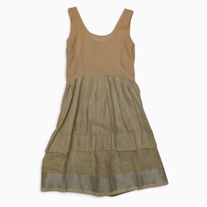 Peut inclure: Une robe sans manches avec un corsage beige à encolure dégagée et une jupe froncée à étages de couleur vert olive. La jupe présente une large bande argentée métallique le long de l'ourlet inférieur, créant un contraste avec les tons terreux.