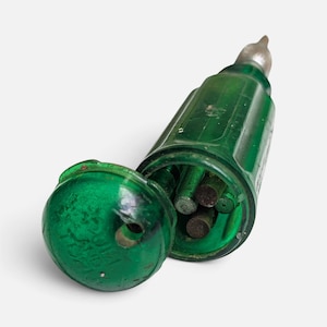 May include: A translucent emerald green plastic tool handle with a hinged cap, containing several dark metal rods inside. The handle features a ribbed cylindrical body and a rounded top with embossed text, topped with a silver metal tip.
