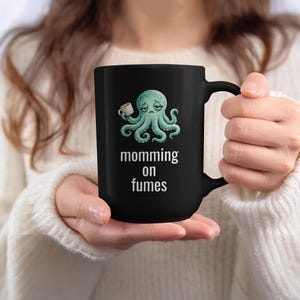 mug with exhausted cartoon octopus with an empty coffee mug featuring the phrase "momming on fumes".