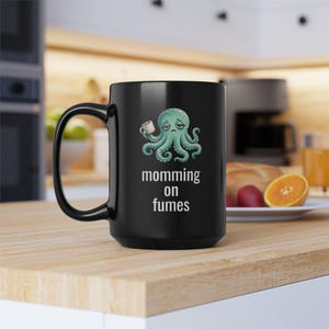 mug with exhausted cartoon octopus with an empty coffee mug featuring the phrase "momming on fumes".