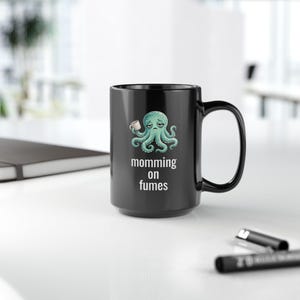 mug with exhausted cartoon octopus with an empty coffee mug featuring the phrase "momming on fumes".
