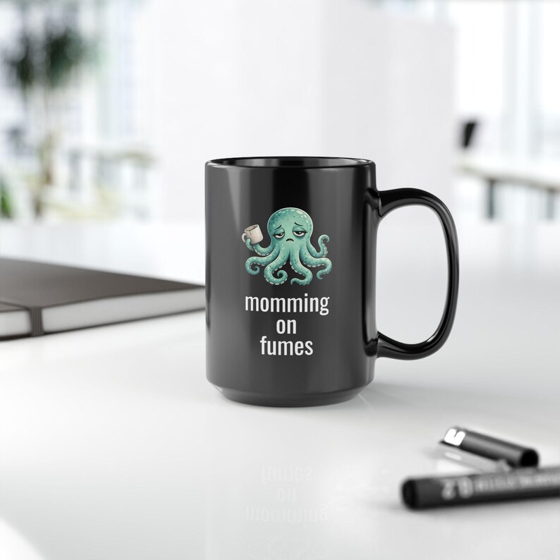 mug with exhausted cartoon octopus with an empty coffee mug featuring the phrase "momming on fumes".