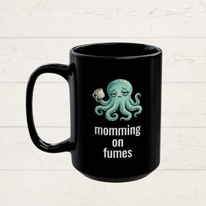 mug with exhausted cartoon octopus with an empty coffee mug featuring the phrase "momming on fumes".