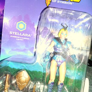 May include: A vintage action figure of Stellara, a warrior from Symbion, packaged on a Sectaurs card. The figure is in a clear plastic bubble, with a blue and purple outfit, blonde hair, and accessories including a shield and weapon.