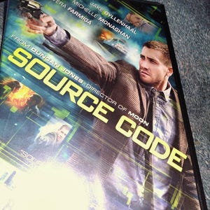May include: DVD case for the movie "Source Code" featuring Jake Gyllenhaal. The cover art shows Gyllenhaal holding a gun, with the title in large yellow letters. Other actors listed include Vera Farmiga and Michelle Monaghan.