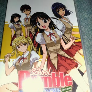 May include: A School Rumble First Semester DVD case featuring an anime illustration of five characters in school uniforms with white shirts, tan vests, and red skirts against a yellow background. The title is printed in large red and white letters.