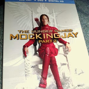 May include: A Blu-ray and DVD combo pack for "The Hunger Games: Mockingjay - Part 2." The cover features a woman in a red outfit seated on a throne, with the film's title in gold lettering. The tagline reads, "Nothing Can Prepare You for the End."