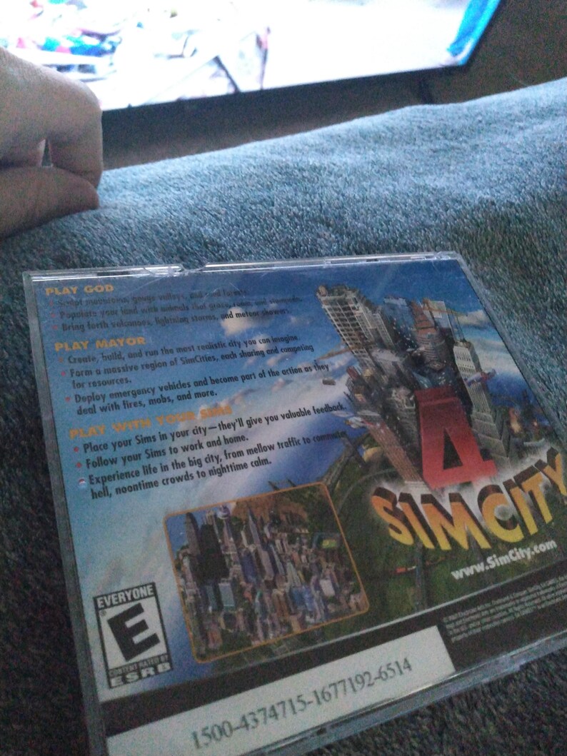 May include: A SimCity PC game case. The cover shows a cityscape with the game's logo. The back of the case has text describing gameplay features, including playing as God or Mayor. The ESRB rating is visible.