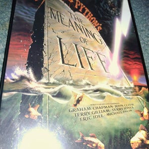May include: A DVD case for Monty Python's The Meaning of Life featuring a large stone monolith rising from dark water. The cover displays the title, a lightning bolt, and several fish with human faces swimming in the foreground, along with cast names.