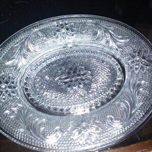 May include: Clear glass serving dish with an oval center and floral and scrollwork embossed design. The dish has a textured surface and a decorative edge, suitable for serving appetizers or desserts.