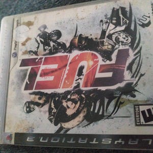 May include: A PlayStation 3 video game case for the game "FUEL". The case features the game's title in large red letters, with a grunge-style background and illustrations of motorcycles and riders. The ESRB rating is "Everyone".