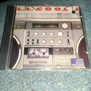 May include: An L.L. Cool J music CD in a clear plastic jewel case. The cover art features a graphic illustration of a vintage grey boombox with a cassette tape deck, various control knobs, and speakers. The text L.L. COOL J is printed at the top.