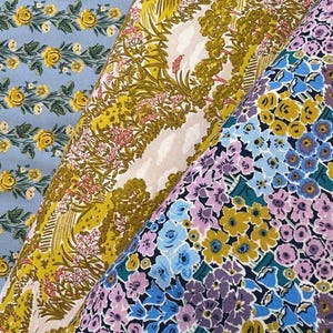 May include: Three fabric swatches with floral patterns. One is light blue with yellow roses, another has a yellow and pink landscape design, and the third features a mix of blue, yellow, and purple flowers.