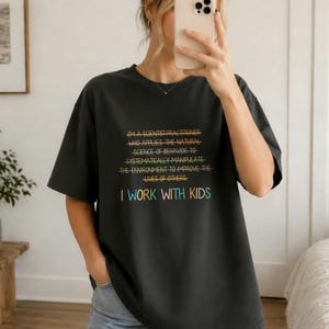 Peut inclure: Un t-shirt gris foncé à manches courtes avec un texte multicolore qui dit : I'M A SCIENTIST PRACTITIONER WHO APPLIES THE NATURAL SCIENCE OF BEHAVIOR TO SYSTEMATICALLY MANIPULATE THE ENVIRONMENT TO IMPROVE THE LIVES OF OTHERS. I WORK WITH KIDS.