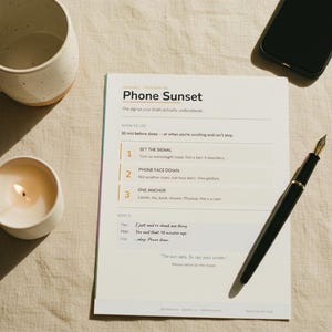 May include: A still-life composition featuring a lit candle, a ceramic mug, a smartphone, and a fountain pen on a beige surface. A printed paper titled "Phone Sunset" is also present, with text about sleep habits.