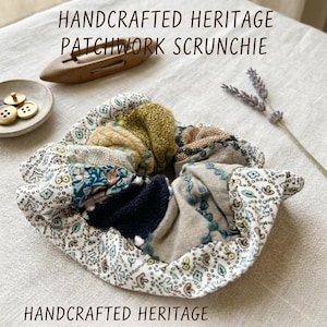Può includere: Un elastico per capelli patchwork fatto a mano con resti di tessuti vintage. L'elastico presenta una varietà di tessuti nei toni del blu, beige, verde e motivi floreali. Il testo "HANDCRAFTED HERITAGE PATCHWORK SCRUNCHIE" è visualizzato.