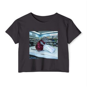 May include: Black crop top with a humorous image of a rat in a red outfit holding a box labelled "Family Overdose Shop" in a pharmacy setting. The image is a parody of a Walgreens store.