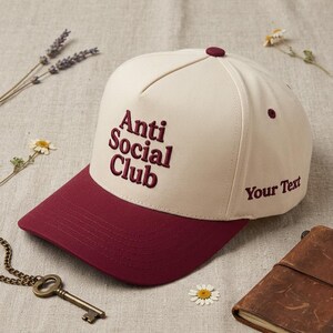 Peut inclure: Casquette de baseball cr&egrave;me et bordeaux avec texte brod&eacute;. Le texte "Anti Social Club" est brod&eacute; &agrave; l'avant et "Your Text" sur le c&ocirc;t&eacute;. Un accessoire de mode pour un look d&eacute;contract&eacute;.