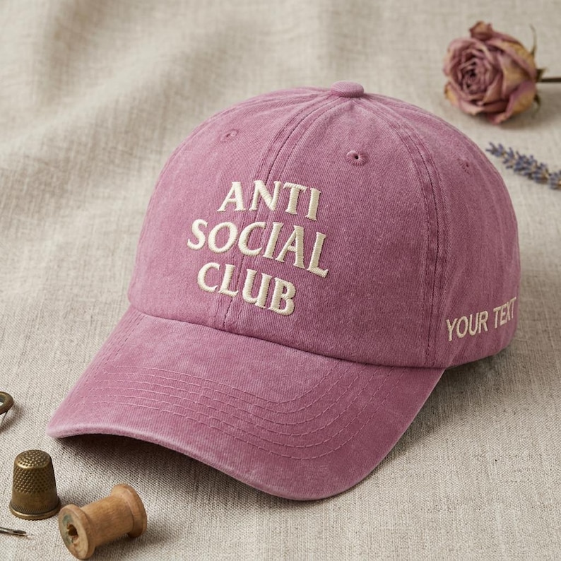 Peut inclure: Casquette de baseball rose poussi&eacute;reux avec les mots "ANTI SOCIAL CLUB" brod&eacute;s en blanc. La phrase "YOUR TEXT" est brod&eacute;e sur le c&ocirc;t&eacute;. La casquette est en tissu doux et textur&eacute;.