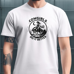 K&ouml;nnte beinhalten: Wei&szlig;es T-Shirt mit einer schwarzen Grafik einer Cowgirl auf einem Pferd, die einen Lasso h&auml;lt, vor einer W&uuml;stenlandschaft. Der Text "COWGIRLS DO IT BETTER" ist kreisf&ouml;rmig um das Bild gedruckt.