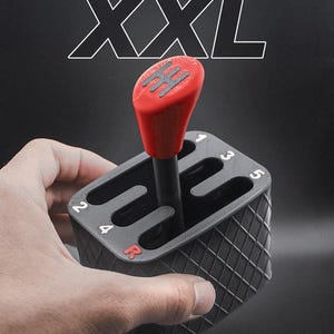 Può includere: Un giocattolo fidget con cambio marcia nero e rosso con la scritta "Gear Shift Fidget Toy XXL". Il giocattolo ha un pomello del cambio rosso e una base nera con fessure per il cambio. La base ha un motivo a diamante.